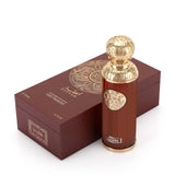 The image features "La Luna" by Gissah, displayed alongside its packaging. The perfume bottle is a sleek copper color with a gold ornate medallion and an intricately designed gold spherical cap. The packaging is a deep brown box with a textured surface and a large gold circular mandala design on the top. The box also has the name "Gissah" and "LA LUNA" along with the description "SIGNATURE COLLECTION LIGHT FRAGRANCE."