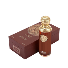 The image features "La Luna" by Gissah, displayed alongside its packaging. The perfume bottle is a sleek copper color with a gold ornate medallion and an intricately designed gold spherical cap. The packaging is a deep brown box with a textured surface and a large gold circular mandala design on the top. The box also has the name "Gissah" and "LA LUNA" along with the description "SIGNATURE COLLECTION LIGHT FRAGRANCE."