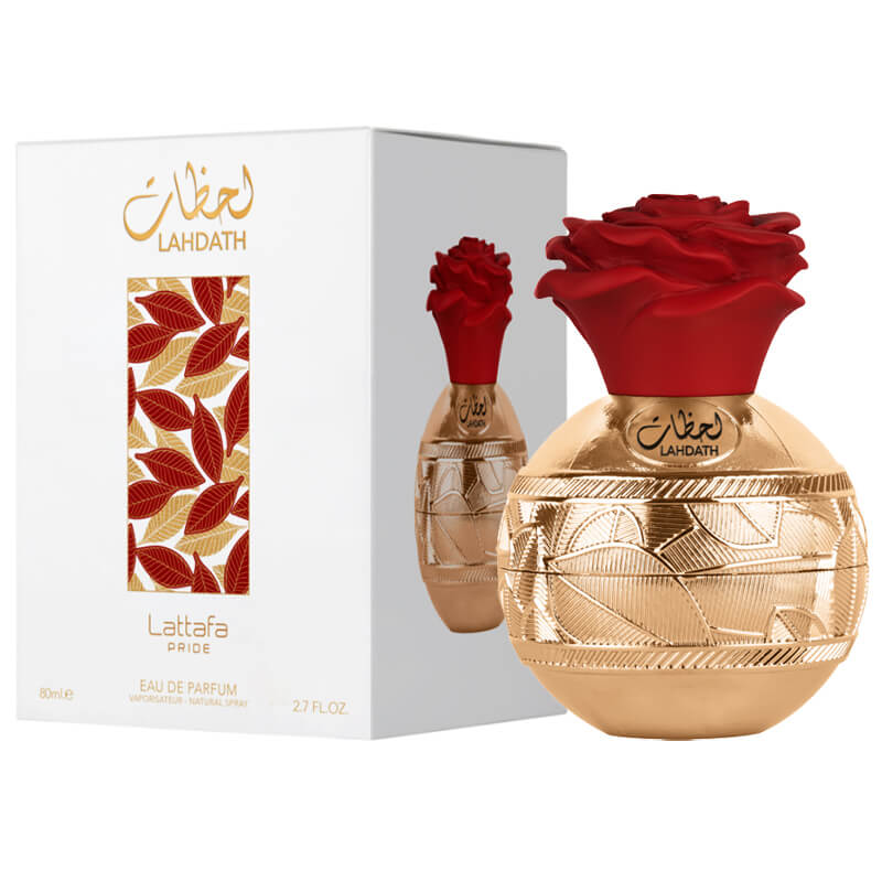 This image displays a perfume bottle and its box. The bottle has a spherical gold base with intricate, geometric patterns and is topped with a large, red rose-shaped cap. On the front of the bottle in both Arabic and Latin script is the word "LAHDATH," al
