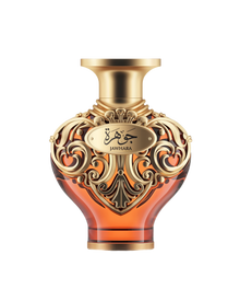 A product shot of Le Falcone Niche Collection’s “Jawhara” perfume bottle against a white background: a heart-shaped amber glass vessel topped with a wide, gold-tone cap. The bottle’s upper half is wrapped in ornate gold filigree with elegant arabesque scrollwork, featuring an oval plaque engraved with Arabic calligraphy above the word “Jawhara.”