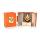 A product shot of Le Falcone Niche Collection’s “Jawhara” perfume against a white background: on the left, a closed matte-orange rectangular gift box with a metallic gold plaque displaying Arabic calligraphy above the word “Jawhara” and the Le Falcone logo; on the right, the same box opened to reveal a heart-shaped amber glass bottle nestled on a raised beige interior platform. The bottle’s upper half is wrapped in intricate gold-tone filigree scrollwork, with an oval plaque with matching Arabic script.
