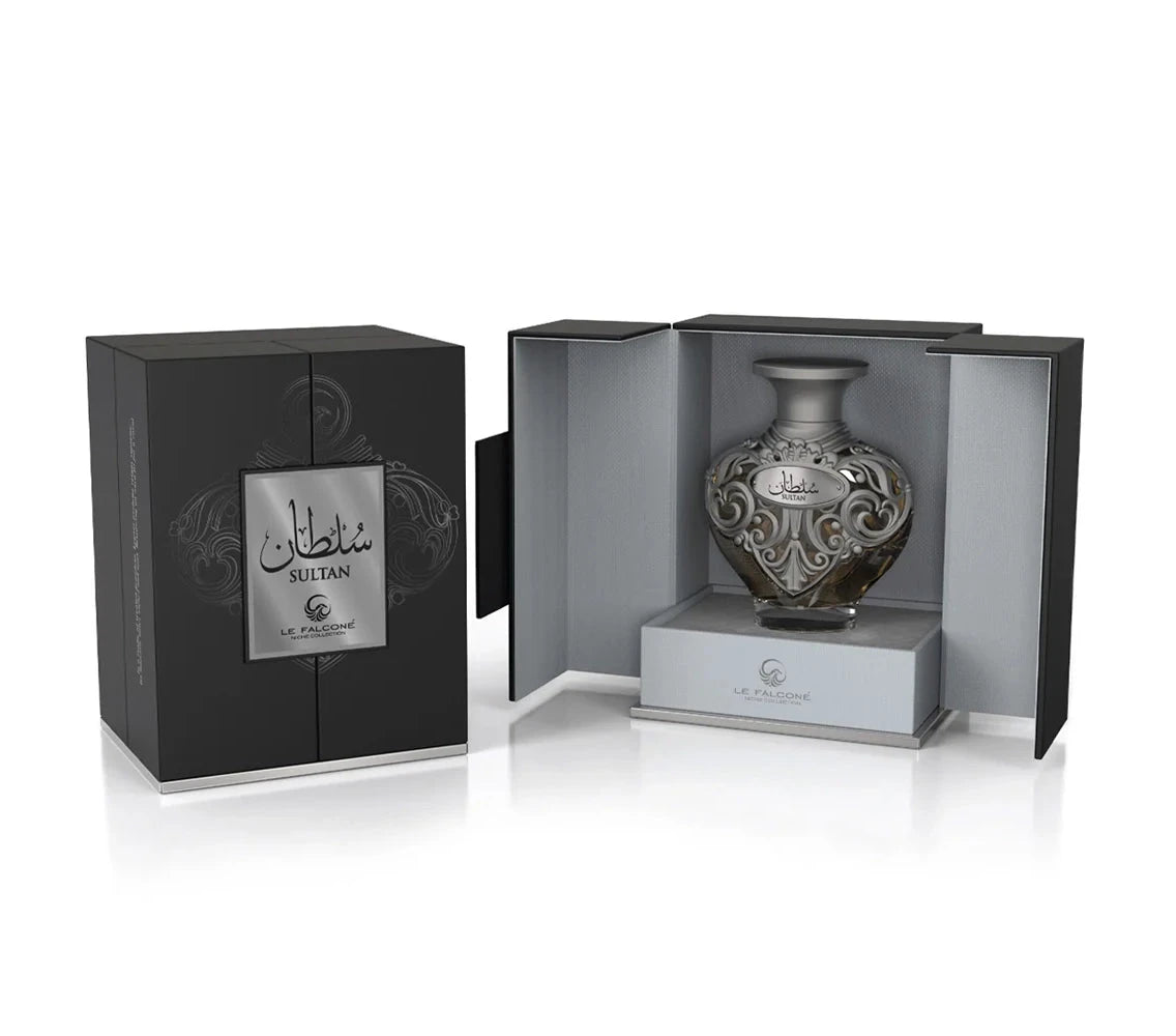 A product shot of Le Falcone’s “Sultan” niche-collection perfume: a matte black rectangular gift box with a silver plaque bearing Arabic script and the word “Sultan” sits closed on the left. On the right, the box is open to reveal an ornate, heart-shaped glass perfume bottle adorned with intricate silver filigree and a matching “Sultan” label, nestled on a light grey interior platform.
