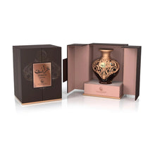 A product shot of Le Falcone Niche Collection’s “Turath Intense” perfume against a white background: on the left is a closed, matte dark-brown rectangular gift box with a copper foil plaque bearing Arabic calligraphy above the words “Turath Intense” and the Le Falcone logo. On the right, the box is open to reveal a heart-shaped amber glass bottle resting on a raised copper-pink interior platform.