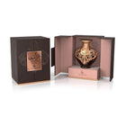 A product shot of Le Falcone Niche Collection’s “Turath Intense” perfume against a white background: on the left is a closed, matte dark-brown rectangular gift box with a copper foil plaque bearing Arabic calligraphy above the words “Turath Intense” and the Le Falcone logo. On the right, the box is open to reveal a heart-shaped amber glass bottle resting on a raised copper-pink interior platform.