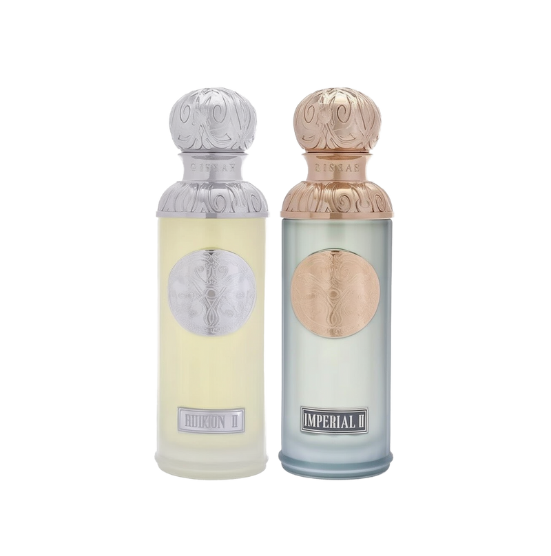 The image features two perfume bottles from the Gissah collection, "Hudson II" and "Imperial II." Both bottles have tall, cylindrical shapes with ornate silver caps featuring embossed designs. "Hudson II" has a light yellow tinted glass body with a silver medallion, and "Imperial II" has a light blue tinted glass body with a copper medallion. Each bottle is labeled with its respective name in elegant font at the bottom. 