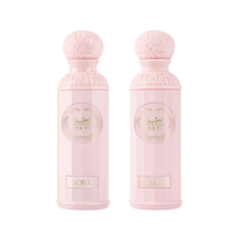 The image features two light pink perfume bottles from the "Legend of the Sky for Her" collection by Gissah, named "Sora" and "Ellora." The bottles have a cylindrical shape with detailed ornamental designs embossed on the silver caps and the central gold medallions. The names "Sora" and "Ellora" are inscribed on gold plaques at the base of each bottle. 