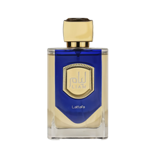 The image features a bottle of Liam Blue Shine perfume by Lattafa. The bottle has a clear, rectangular glass base with a blue color gradient at the top half. It features a prominent gold label with a textured border and the name "Liam" in stylized font in the center. Below the label, the word "Lattafa" is printed in small, simple white letters. The cap of the bottle is a smooth, metallic gold color with a faceted design, giving it a luxurious and elegant appearance.