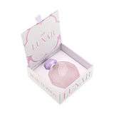A pastel pink octagonal perfume bottle with intricate embossed designs on the front, nestled inside an open white and pink box. The bottle features a matching pastel purple cap and a silver collar. The box is labeled "Lunar Musk Edition" with the Gissah brand name and the phrase "Illuminate Your Senses with Lunar." The interior and exterior of the box are decorated with elegant patterns that complement the delicate and luxurious appearance of the bottle.
