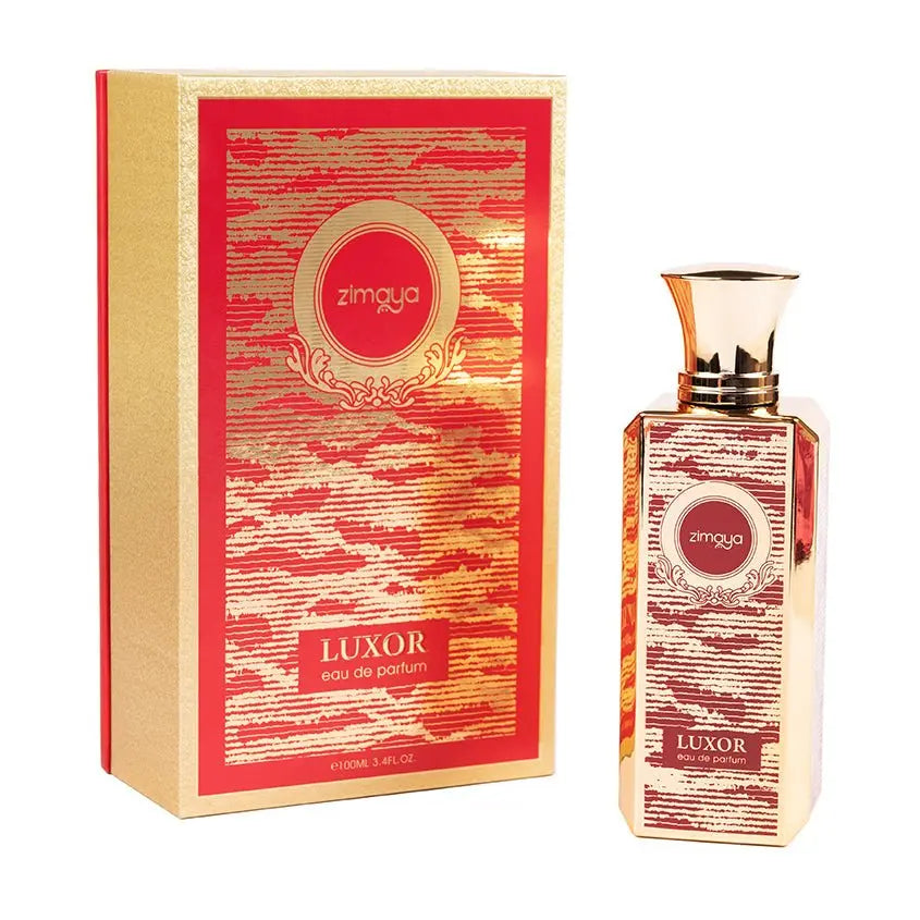 The image shows a bottle of "Luxor" eau de parfum by Zimaya alongside its packaging. The perfume bottle is tall and rectangular with a gold cap, featuring an ornate red and gold label with the brand name "zimaya" in a circular emblem near the top. The word "Luxor" is written in bold at the bottom of the label, along with "eau de parfum." The packaging box matches the bottle's design, with a red and gold pattern and similar branding elements.