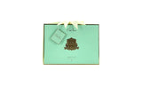 A mint green luxury gift box from Cote Noire adorned with a gold emblem and a matching gold-trimmed label. The box features a cream-colored ribbon tied at the top with a small tag that reads 'Cote Noire.' The text on the box indicates it contains floral, candle, and diffuser products.