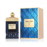 The image shows a product which appears to be a perfume named "Sapphire Leather" by Ibraheem Al Qurashi. It includes a dark blue glass bottle with a textured design on the lower half and a gold-colored neck and cap. There is a label on the bottle with the name of the perfume in both English and Arabic script. Beside the bottle is a box with a blue textured pattern and a gold label that matches the bottle's label. The box has a beige side panel, suggesting a three-dimensional perspective. 