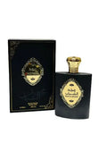 The image depicts a perfume set which includes a matte black bottle and its corresponding packaging box. The bottle has a gold label with intricate scrollwork and Arabic calligraphy in the center, which is consistent with the design on the box. The cap of the bottle is a textured gold, with a shape resembling a traditional dome or a royal crown. The box mirrors the bottle's aesthetic, with a similar gold label and calligraphy on a glossy black background. 