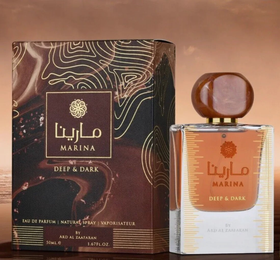 The image shows a perfume product named "Marina Deep & Dark" by Ard Al Zaafaran. The perfume bottle is rectangular with a golden brown cap and has Arabic and English text printed on it. The packaging box is dark with intricate golden patterns and a label in the center that displays the brand name "Marina" in both Arabic and English, along with the description "Deep & Dark".