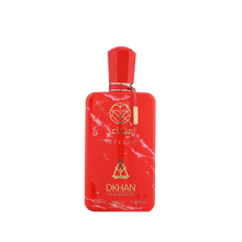 This is an image of a bold red perfume bottle with white marble-like patterns. The bottle has a geometrically shaped cap and a gold-colored label attached to the front. The label features the word "club" in lowercase letters followed by "INTENSE" in uppercase. Below, there is a logo comprising a heart inside a diamond shape and the text "DKHAN FRAGRANCES." 