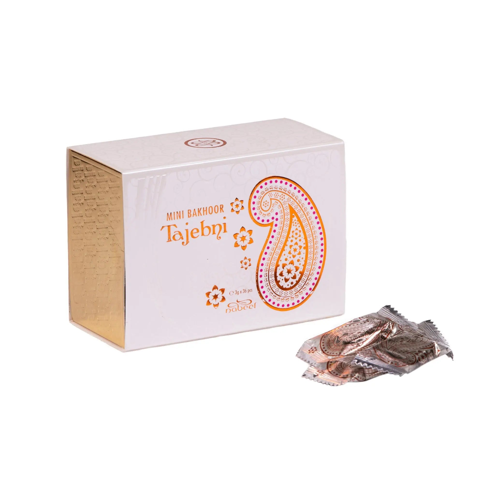 The image shows a white box for "Mini Bakhoor Tajebni" by Nabeel Perfumes. The box has a large paisley design in shades of orange and pink on the front, along with the product name in both English and Arabic. The left side of the box is gold with embossed Arabic script. Next to the box are several small, sealed packets with an orange and brown color scheme that matches the box's design. These packets likely contain the bakhoor incense pieces.