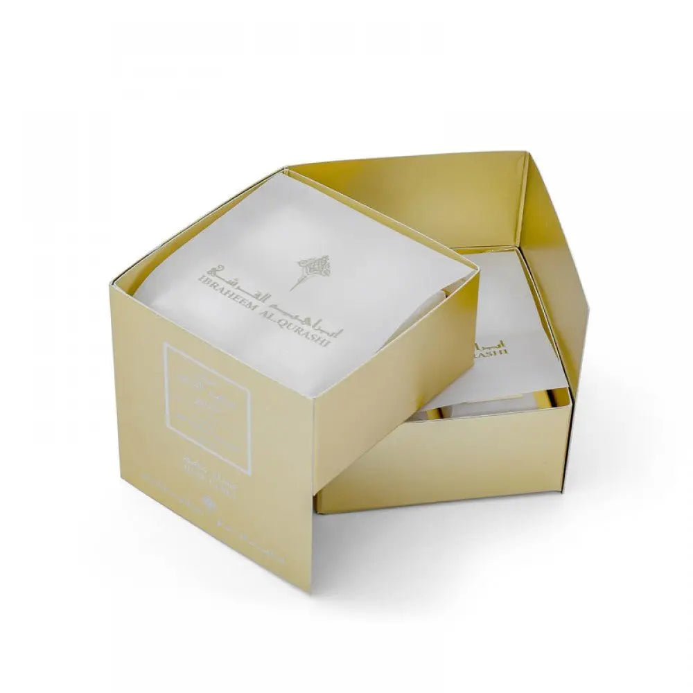 The image displays an open, gold-colored square packaging box with a smaller inner box visible inside. The inner box is white with the logo and name "Ibraheem Al Qurashi" in both Arabic and English, also stating "Musk Cubes Special". The exterior of the open box features a minimalistic design with a smaller, embossed square and text, enhancing the luxurious feel of the product packaging.
