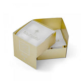 The image displays an open, gold-colored square packaging box with a smaller inner box visible inside. The inner box is white with the logo and name "Ibraheem Al Qurashi" in both Arabic and English, also stating "Musk Cubes Special". The exterior of the open box features a minimalistic design with a smaller, embossed square and text, enhancing the luxurious feel of the product packaging.