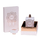 The image shows a bottle of "Musk Is Great" extrait de parfum by Noya alongside its packaging. The perfume bottle is rectangular and white, featuring intricate geometric designs in metallic rose gold. The bottle has a distinctive, square-shaped cap with vertical ridges and a rose gold accent at the base, which is placed next to the bottle in the image. The bottle is shown standing in a matching rose gold-lined tray, enhancing the luxurious and elegant presentation of the product.