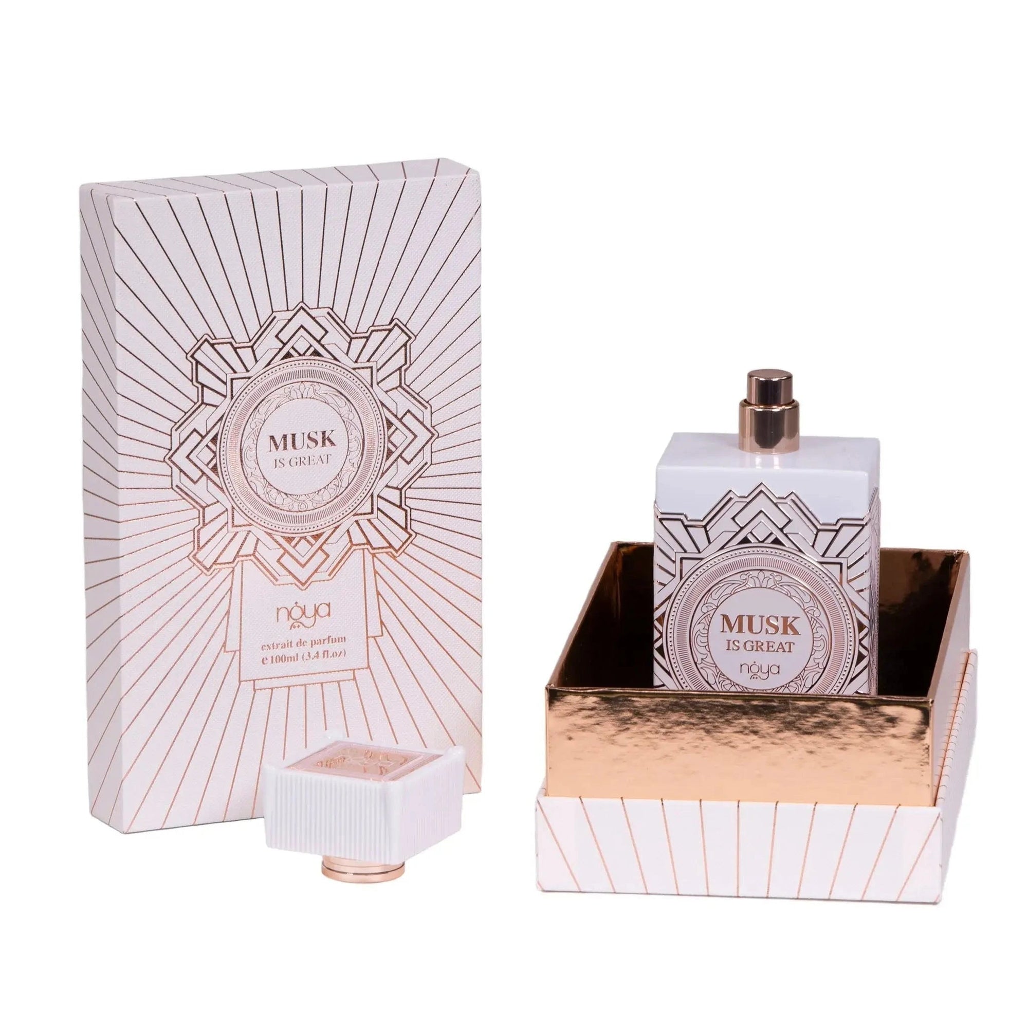 The image shows a bottle of "Musk Is Great" extrait de parfum by Noya alongside its packaging. The perfume bottle is rectangular and white, featuring intricate geometric designs in metallic rose gold. The bottle has a distinctive, square-shaped cap with vertical ridges and a rose gold accent at the base, which is placed next to the bottle in the image. The bottle is shown standing in a matching rose gold-lined tray, enhancing the luxurious and elegant presentation of the product.
