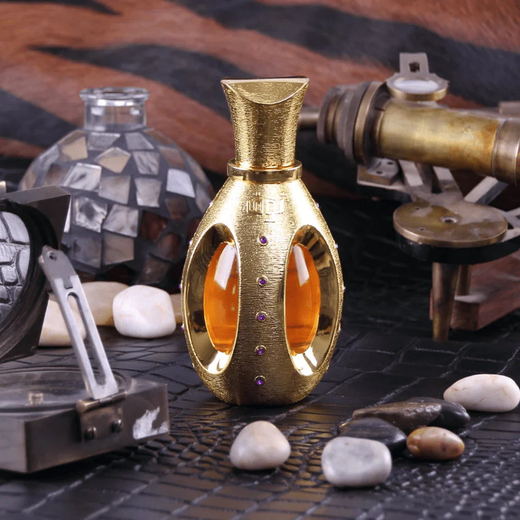 The image features a textured gold perfume bottle with an ornate design and purple gemstone embellishments, placed on a textured surface with an assortment of objects that suggest a vintage or exploratory theme. These objects include a compass, some stones, and what appears to be part of a telescope or nautical equipment, all contributing to a sense of adventure or discovery. 