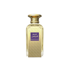 The image is of a perfume bottle with a rich golden color and textured design. The bottle has a rectangular shape with a curved top and a broad, flat base. The cap is a smooth, polished gold matching the bottle's texture. On the front, there is a purple label with Arabic script, which translates to "Naseej Al Khuzama," indicating the name of the fragrance. The text below the Arabic script, in smaller font, is the English transliteration of the name.