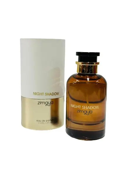 The image shows a bottle of "NIGHT SHADOW" eau de parfum by Zimaya, alongside its packaging. The perfume bottle is made of a dark amber glass with a black cap, and the product name is written in a minimalist white font across the lower half. Beside it is the cylindrical packaging, which fades from white at the top to a golden color matching the lower section of the bottle. 