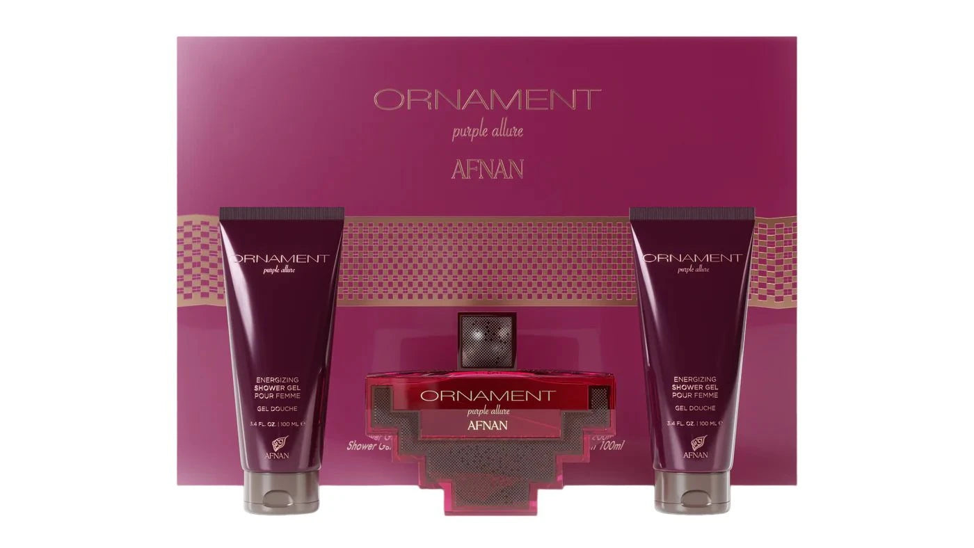 The image shows a beauty product set by AFNAN called "ORNAMENT purple allure". It includes two deep purple colored tubes labeled as "ENERGIZING SHOWER GEL POUR FEMME" and a matching perfume bottle in the center. The bottle has a square base with a red body and a cross-shaped metallic silver design embracing it. The cap appears to be a silver metallic color as well. Behind the products is a large cardboard packaging with the same deep purple color and a textured pattern.
