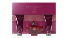The image shows a beauty product set by AFNAN called "ORNAMENT purple allure". It includes two deep purple colored tubes labeled as "ENERGIZING SHOWER GEL POUR FEMME" and a matching perfume bottle in the center. The bottle has a square base with a red body and a cross-shaped metallic silver design embracing it. The cap appears to be a silver metallic color as well. Behind the products is a large cardboard packaging with the same deep purple color and a textured pattern.