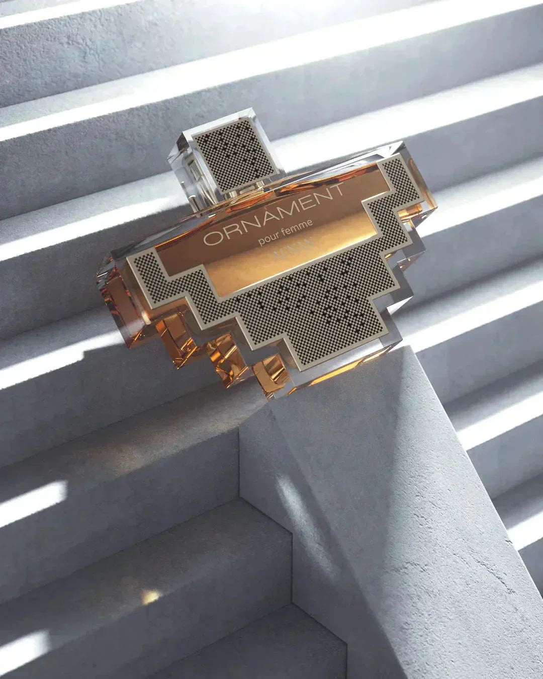 The image displays an intricately designed perfume bottle with a clear geometric shape, resting on a set of concrete stairs. The bottle has a transparent and gold color scheme, with sections of silver mesh pattern.  The bottle is positioned in such a way that it catches the sunlight filtering through blinds, casting linear shadows that complement the bottle's angular design, adding to the visual appeal and suggesting a modern, sophisticated product.
