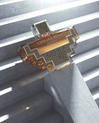 The image displays an intricately designed perfume bottle with a clear geometric shape, resting on a set of concrete stairs. The bottle has a transparent and gold color scheme, with sections of silver mesh pattern.  The bottle is positioned in such a way that it catches the sunlight filtering through blinds, casting linear shadows that complement the bottle's angular design, adding to the visual appeal and suggesting a modern, sophisticated product.