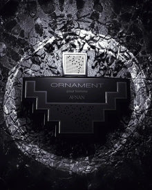 The image displays a monochrome perfume bottle with a distinctive geometric shape set against a textured, dark background resembling cracked stone or dried earth. The bottle is black with silver details and features a label with the text "ORNAMENT pour homme AFNAN," specifying that it is a men's fragrance from the brand AFNAN. The bottle cap has a mesh pattern, which adds to the overall modern and masculine aesthetic of the image. 