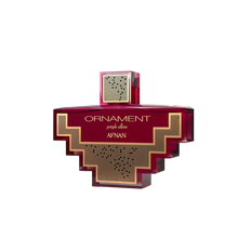 The image shows a perfume bottle with a distinctive design. The bottle is a deep purple color with a complex, geometric shape reminiscent of an ornament or a cross with stepped arms extending from the central square. The center of the bottle features a patterned gold grid design that contrasts with the purple. The cap is square and mirrors the same gold grid pattern. 