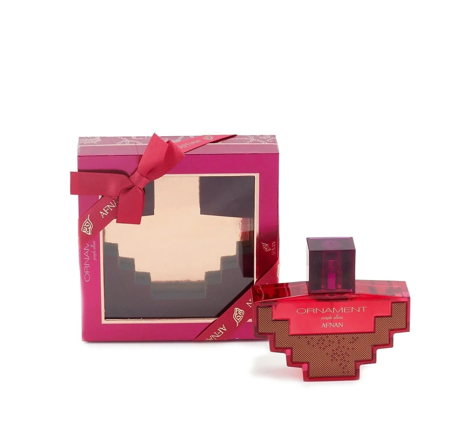 The image displays a perfume set that includes a bottle and its packaging. The perfume bottle has a unique cross-like shape with a geometric design in a translucent red hue with a gold patterned design in the center. The cap is a darker shade of red and square in form. The text on the bottle reads "ORNAMENT purple allure AFNAN." Accompanying the bottle is a square packaging box in a rich purple color with a transparent window wrapped with a satin ribbon in a bow, showcasing the bottle inside. 