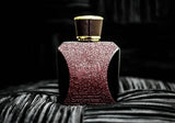 The image presents an artistically shot perfume bottle placed on a textured surface. The bottle is a rich burgundy color with a textured pattern that appears to be embossed on its surface, giving a luxurious and tactile appearance. It has a rounded square shape with a gold cap that has a leather-like texture, complementing the elegance of the bottle design. The bottle features Arabic calligraphy in a slightly deeper tone than the bottle itself, creating a subtle and sophisticated look.