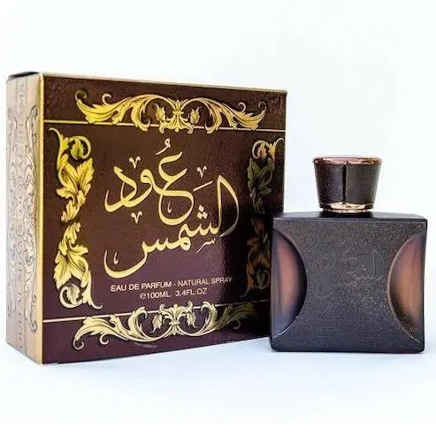 The image shows a perfume set that includes a square-shaped, matte black bottle with rounded corners and a rose gold cap, alongside its packaging. The box is dark, almost black, with ornate golden and green decorative elements framing the central Arabic calligraphy and the text "Eau de Parfum - Natural Spray 100ml - 3.4 fl.oz" in English. The design elements give the product a luxurious and traditional aesthetic.