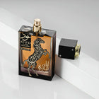The image presents "Oud Lail Maleki" by Lattafa, a perfume bottle with a unique design. The bottle has a dark, amber glass with a rearing horse and Arabic calligraphy in white and gold, creating an ornate contrast. The name of the fragrance is written in both Arabic and English. The cap of the bottle is black with gold trim and appears to be detached, revealing a gold-colored spray nozzle. This perfume is presented on a reflective surface with a white backdrop, adding to the luxurious feel of the product.