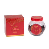 The image features "OUDH Fattan" by Nabeel, which includes a red and gold box with ornate, traditional Arabic-style patterns and a round, clear glass jar with a red lid. The jar has a label with the same design as the box, displaying the name "OUDH Fattan" in both Arabic and English script. The jar and the box have a luxurious appearance, suggesting that they contain a high-quality aromatic product.