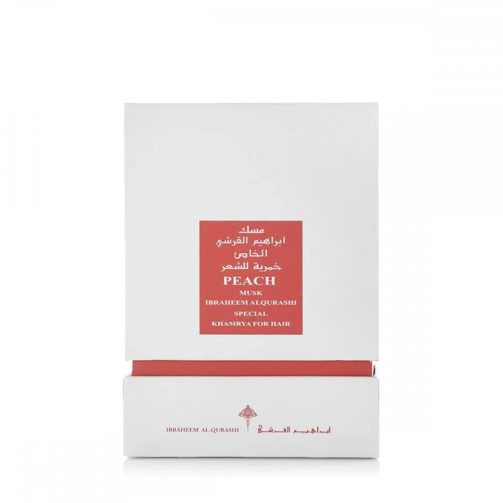 The image displays a white packaging box with a red label for a fragrance product. The label includes the name "PEACH MUSK" in English, with corresponding Arabic script above it. Below, it states "IBRAHEEM AL.QURASHI SPECIAL KHAMRIYA FOR HAIR." A red strip at the box's base matches the label, and the brand's logo is printed in red at the bottom.