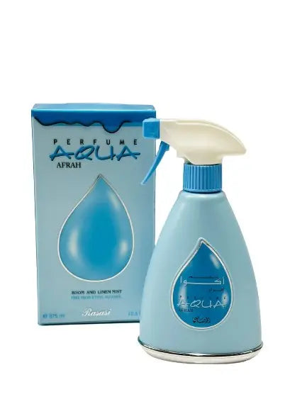 The image displays a room and linen mist spray bottle with its packaging box. The spray bottle is a soft blue color with a white spray nozzle and a blue actuator. It features a teardrop-shaped transparent window that showcases the name "AFRAH" in both Arabic and English scripts within a darker blue teardrop background.  The packaging box mirrors the bottle's color and design, with a blue background and a wavy top edge. It has the text "PERFUME AQUA AFRAH" along with "ROOM AND LINEN MIST 375 ml." 
