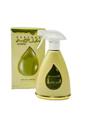 The image features a room and linen mist spray bottle alongside its packaging. The bottle is a light gold color with a white spray nozzle and a teardrop-shaped transparent window that displays the name "AZAMAH" in Arabic script and "AQUA" in Latin script. The accompanying box is yellow with a teardrop motif and the words "PERFUME AQUA AZAMAH" along with "ROOM AND LINEN MIST" and a volume indication of "375 ml." 