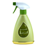 The image shows a light green, teardrop-shaped spray bottle for "AZAMAH" perfume, part of the AQUA series. The bottle has a white spray nozzle with a green actuator. A teardrop-shaped window on the bottle displays the name "AZAMAH" in Arabic script and "AQUA" in Latin script, set against a darker green backdrop with additional decorative script. The base of the bottle is a slightly darker shade of green, providing a gentle contrast to the main body. 