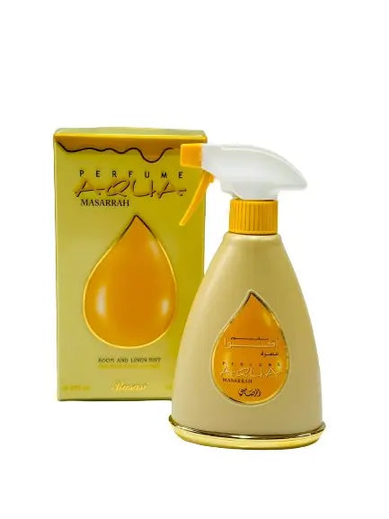 The image features a perfume spray bottle and its packaging box. The bottle has a unique teardrop shape with a golden color and a white spray nozzle with a yellow actuator. It has a label with Arabic calligraphy and English text that reads "MASARRAH" along with smaller text below. The box is yellow with a teardrop design to match the bottle, and it has the text "PERFUME" and "MASARRAH" as well as "ROOM AND LINEN MIST" on it. 