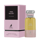 A pink rectangular box labeled ‘Pink Velvet Eau De Parfum’ by Maison Alhambra, displayed beside a tall, cylindrical perfume bottle featuring a metallic swirl cap and a yellow-to-pink color gradient.