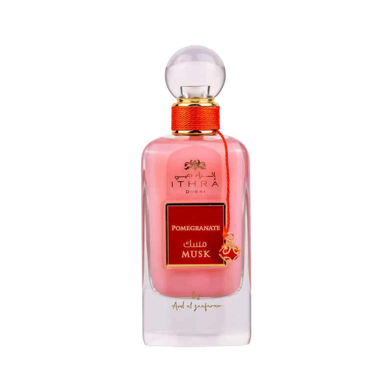 A bottle of Ithra Dubai Pomegranate Musk perfume by Ard Al Zaafaran. It features a clear glass design with a white gradient base and a round glass cap. The perfume liquid has a soft pink hue, and there's a gold-colored brand emblem at the top, with the name of the scent on a red and gold label in the center. A small gold charm with intricate detailing is attached to the neck of the bottle with a red string. The presentation suggests a feminine and luxurious fragrance.