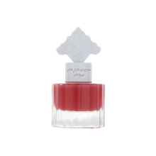 The image shows a perfume bottle with a red liquid and a white cap that has an intricate arabesque design. The label on the bottle, likely in Arabic, suggests that it is a fragrant product intended for hair, possibly part of a special collection by Ibraheem Al.Qurashi. The clear bottom half of the bottle allows the rich red color of the liquid to be prominently displayed, indicating a pomegranate-themed fragrance. The overall design is minimalistic yet elegant.