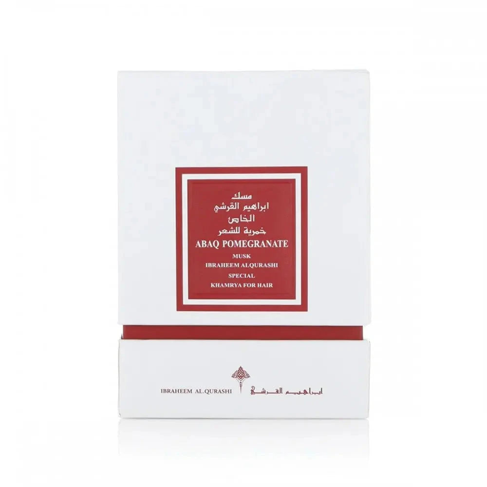 The image displays a white square box with a deep red label framed in gold, indicating a luxury hair product named "ABAQ POMEGRANATE MUSK" by Ibraheem Al Qurashi. This product appears to be part of a special "KHAMRIYA" collection for hair care. The text on the box is likely in both Arabic and English, denoting an exclusive or premium range. 