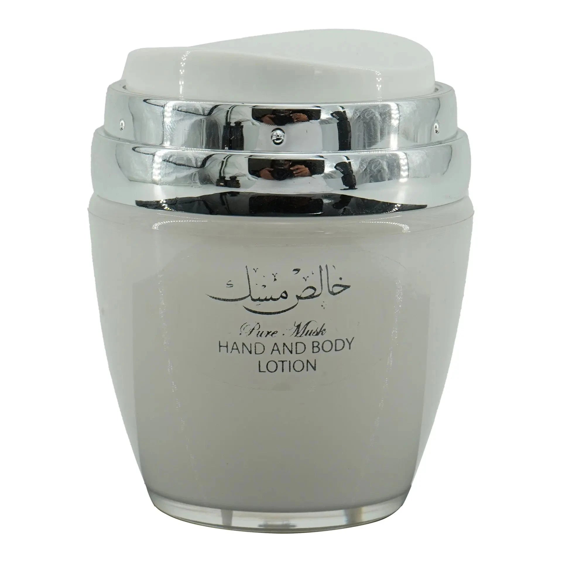 The image features a jar of "Pure Musk" hand and body lotion. The jar is a light gray color with a silver and transparent lid. On the front of the jar, there's a label with Arabic calligraphy at the top and the English words "Pure Musk HAND AND BODY LOTION" printed below. The jar's design is simple yet elegant, with the shiny silver accents of the lid adding a touch of sophistication.