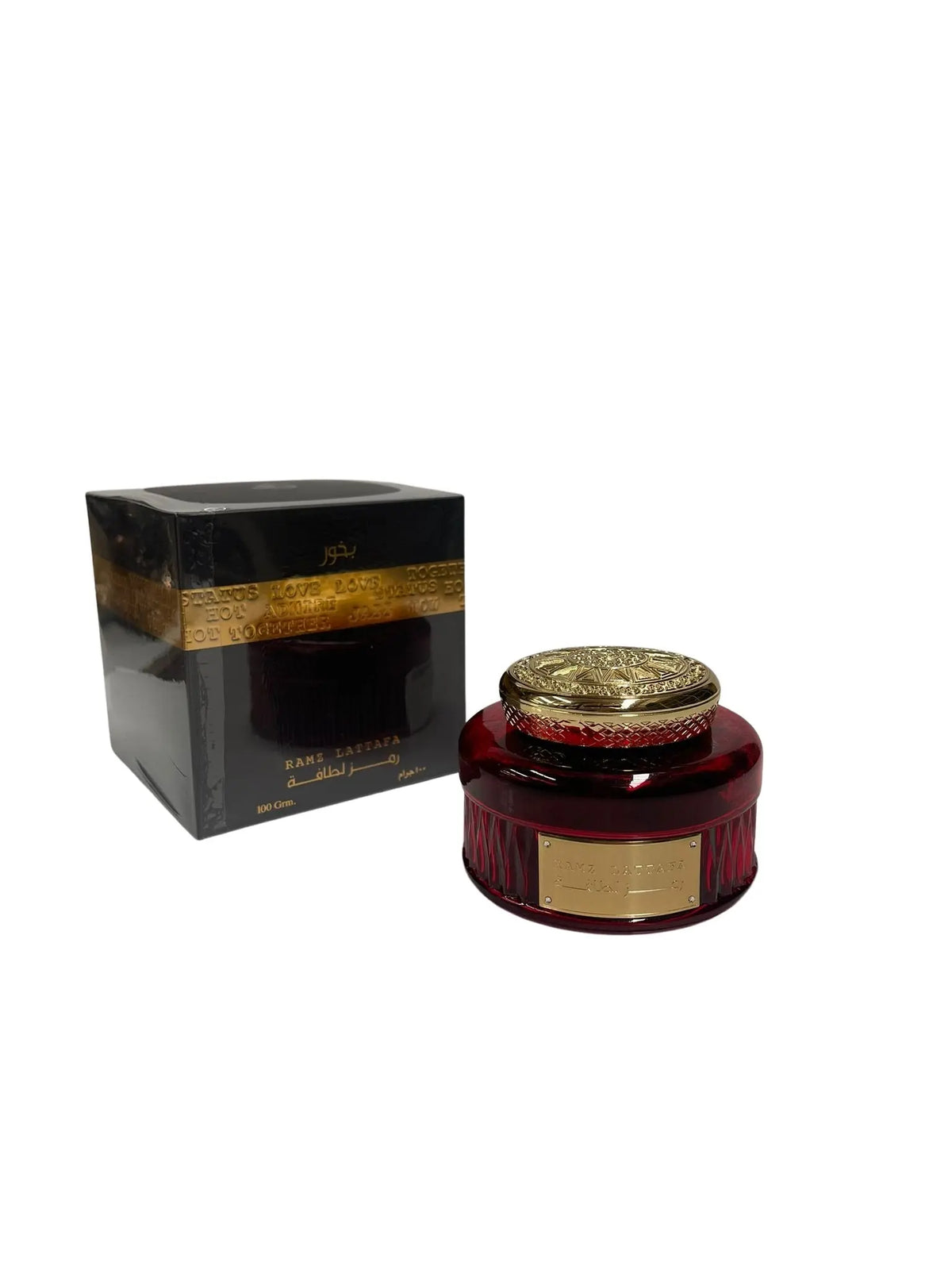 The image features the Ramz Lattafa Bakhoor by Ard Al Zaafaran. The product includes a square box and a container. The box is black with a transparent section revealing golden text, likely describing the fragrance, and a solid black cap. On the box, the product name "RAMZ LATTAFA" is visible in white Arabic script along with "100 Grm." To the side is the bakhoor container, which has a rich burgundy color with vertical ridges and a metallic gold label with the product name in Arabic and English.