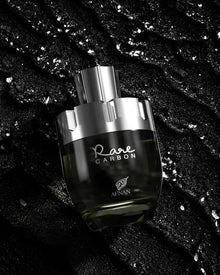 The image depicts a perfume bottle from the brand AFNAN, specifically the "Rare CARBON" fragrance. The bottle has a sleek, modern design with a transparent glass body that fades from clear to a dark gradient at the base, suggesting the color of the perfume within. The bottle is placed against a textured black background with sparkling silver flecks scattered throughout, giving the impression of a luxurious and elegant product. 
