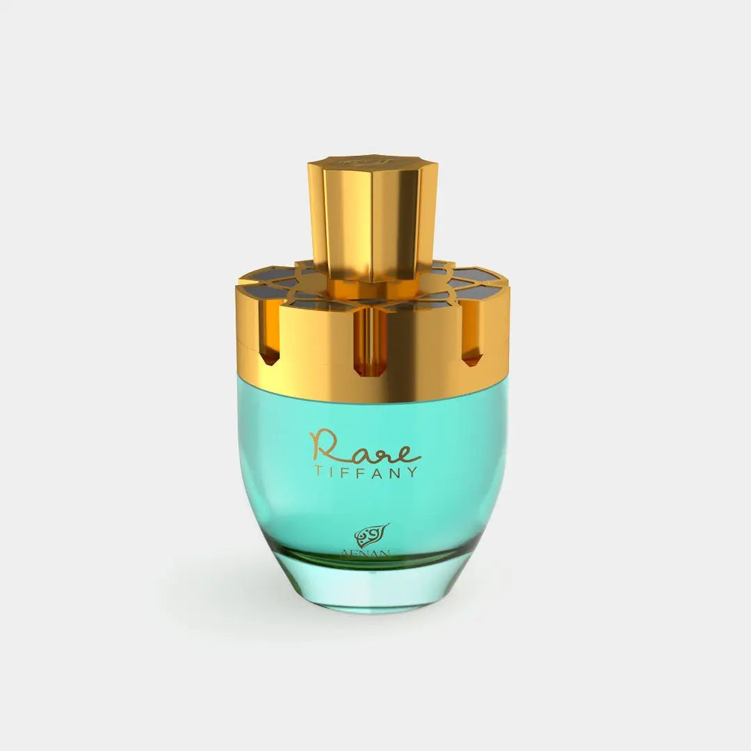 The image features a luxurious perfume bottle. The bottle has a rounded shape with a robust base, tapering slightly towards the top. It is made of translucent teal glass which suggests the perfume inside is of a similar color. The cap of the bottle is a metallic gold, with a geometric, faceted design that gives it a jewel-like appearance. There are gold accents around the neck of the bottle as well, complementing the cap. On the front, in elegant script, the words "Rare Tiffany" are written.